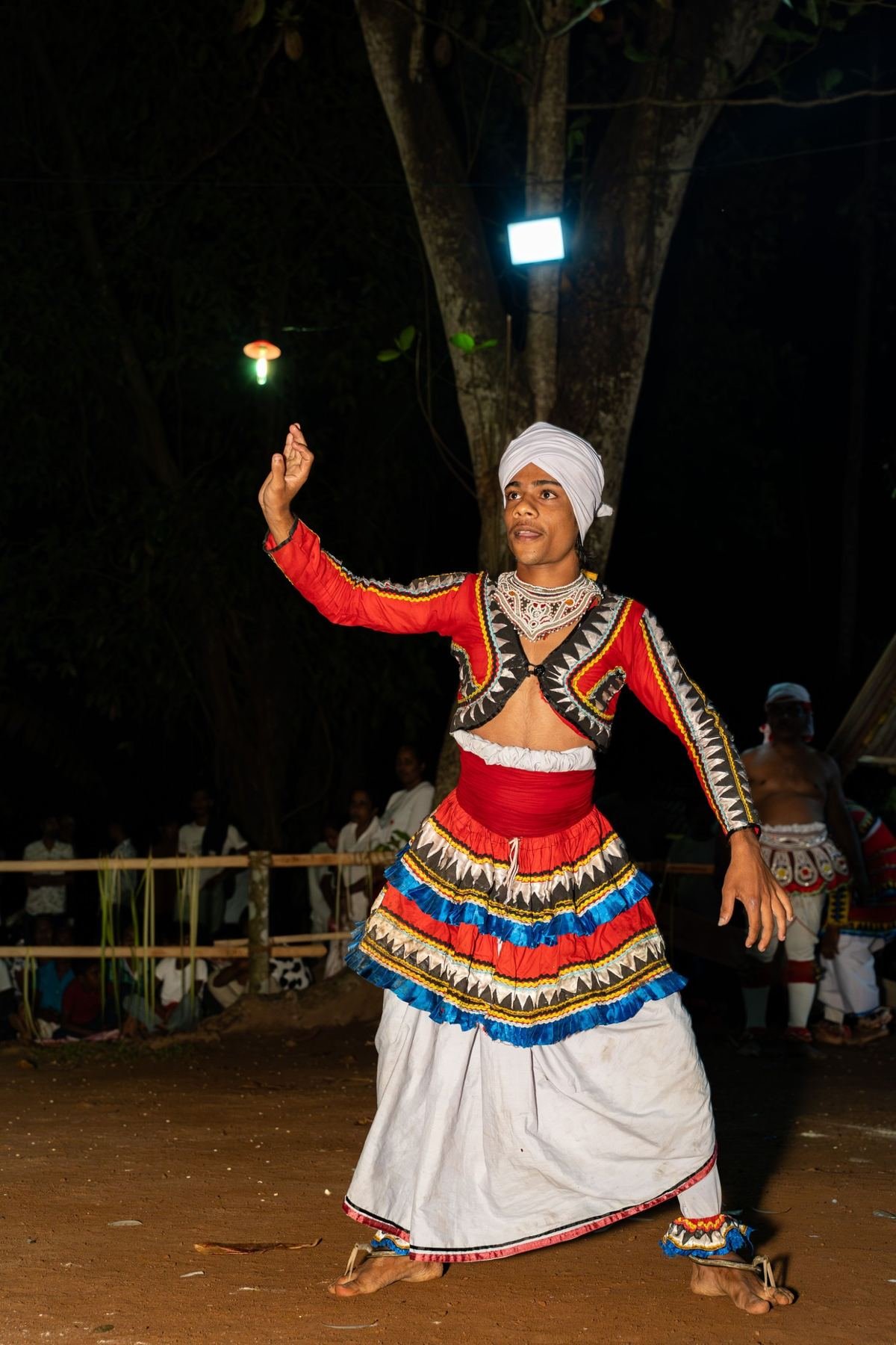 A traditional dancer performing at night beneath a floodlight