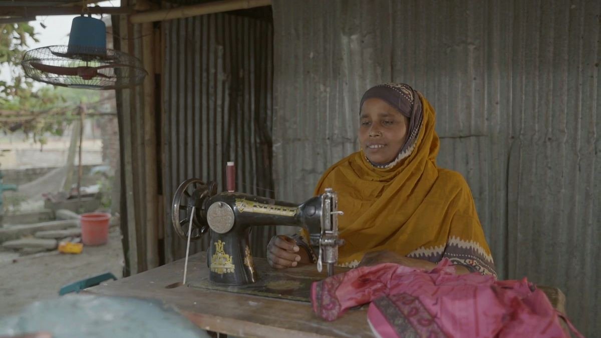 A woman at work at her sewing machine beneath an electric fan
